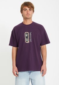 Paarse katoen T-shirt met een centraal grafisch ontwerp en een ingewikkeld ontwerp. Korte mouwen en een losse pasvorm, gecombineerd met lichtblauwe spijkerbroek.