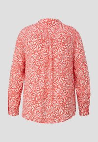 Czerwona bluzka z długim rękawem w białe abstrakcyjne wzory, z kołnierzykiem, guzikami przy mankietach i luźnym krojem. Tył ma marszczone detale.