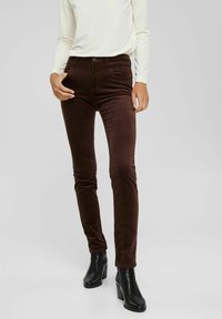 Pantalon skinny en velours côtelé marron avec une taille haute. Comprend un design de poches avant, porté avec des bottines à talons noires et un haut de couleur claire.