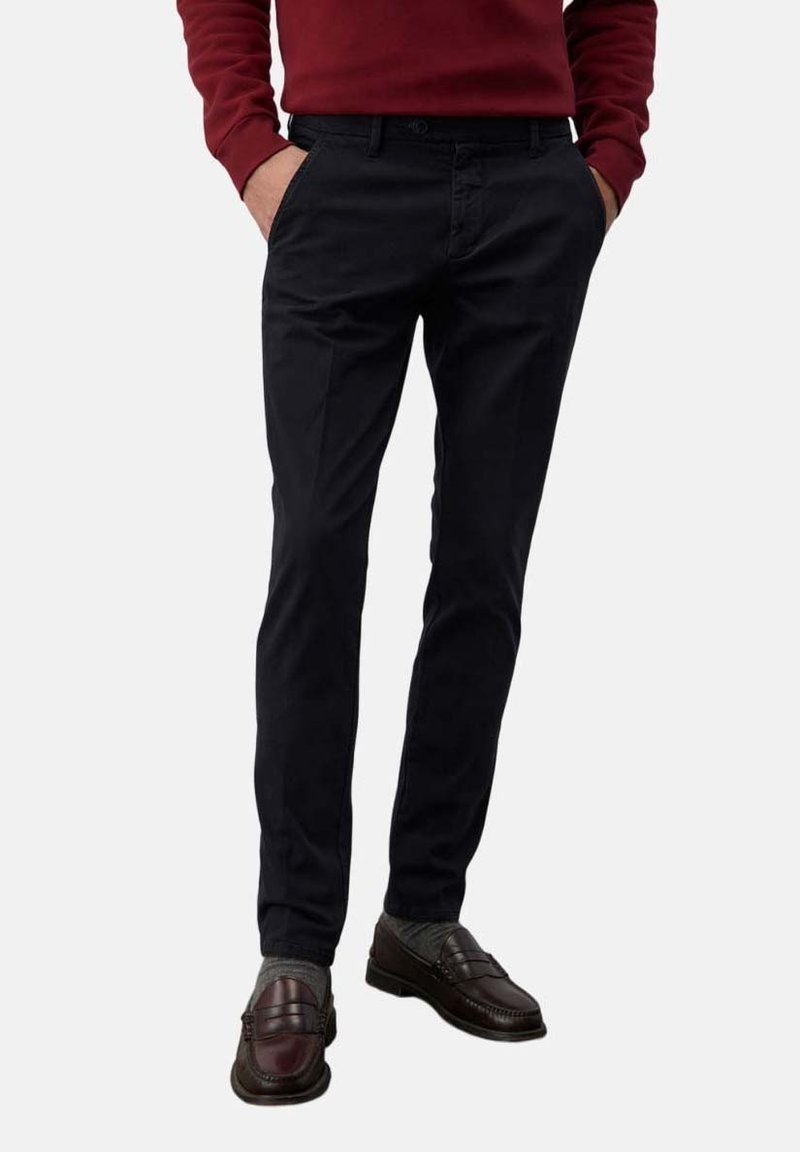 Chino blu navy con vestibilità slim, realizzati in cotone. Presentano tasche laterali e una texture liscia, abbinati a mocassini marroni scuri e calze grigie.