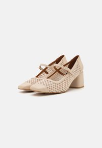 Chaussures à talons beiges avec un dessus en maille texturée, bout pointu et bride croisée. Talon carré pour la stabilité. Embout en cuir lisse.