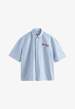 Rövid ujjú, gombos ing világoskék és fehér csíkokkal. A bal mellzseben piros, hímzett "New York" felirattal.