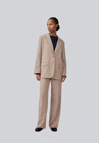 Blazer bege ajustado com um único botão, combinado com calças largas a condizer. Textura suave e design estruturado, acentuado por bolsos.