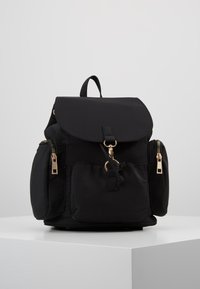 Czarny nylonowy plecak z klapą, złotymi elementami, dwoma bocznymi kieszeniami i zamknięciem na ściągacz; gładka tekstura i minimalistyczny design.