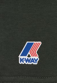 Donkergroene stof met een gestructureerde brei-afwerking, met daarop een wit, blauw en rood K-Way-logo gestikt op het materiaal.