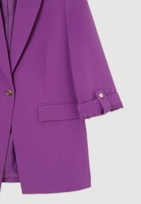 Lila kavaj med skräddarsydd design. Har en enkel knappstängning, vikta manschetter och sidofickor. Slät textur med ett lätt tyg.