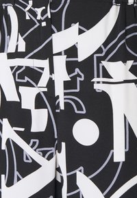 Svart tyg med ett djärvt, abstrakt vitt grafiskt tryck med varierande former, linjer och cirkulära element som skapar ett dynamiskt mönster.