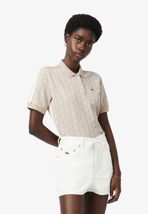 Polo beige con patrón geométrico texturizado, con cuello y tres botones, combinado con pantalones cortos blancos que tienen cordón ajustable y detalle de logotipo.