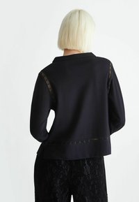 Blusa negra con cuello, con detalles de encaje en los hombros y el dobladillo. Tejido suave con mangas largas y un corte relajado.