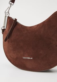 Borsa in suede marrone dalla forma curva, con hardware in argento e dettaglio del logo. Tessuto liscio e una sola tracolla regolabile.