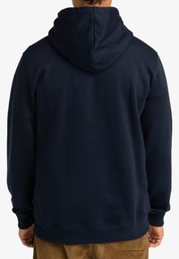 Sudadera con capucha de color azul marino, fabricada con un tejido suave y texturizado, con un bolsillo tipo canguro y puños y dobladillo de canalé. Se muestra la vista trasera.