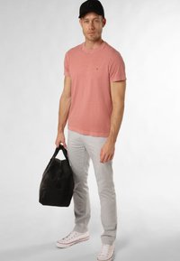 T-shirt rose clair, pantalon gris slim-fit, baskets blanches, sac de sport noir. Tissu doux, design neutre, look décontracté.