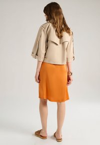 Giacca beige corta con epaulette sulle spalle, gonna arancione al ginocchio e sandali intrecciati marroni. Tessuto morbido e vestibilità comoda.