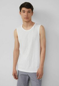 Weißes ärmelloses Tanktop aus leichtem Baumwollmaterial, mit rundem Halsausschnitt und entspannter Passform, getragen mit grauen Hosen. Einfaches Design, keine sichtbaren Muster.