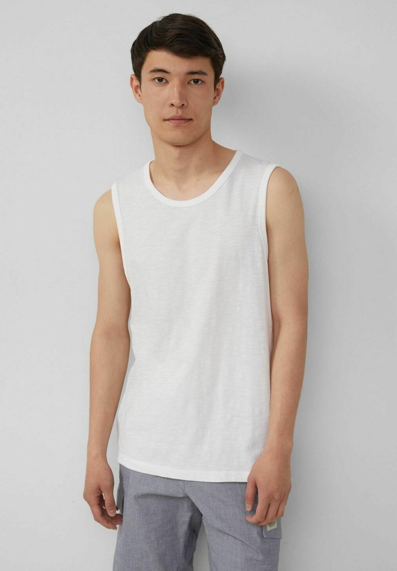Weißes ärmelloses Tanktop aus leichtem Baumwollmaterial, mit rundem Halsausschnitt und entspannter Passform, getragen mit grauen Hosen. Einfaches Design, keine sichtbaren Muster.
