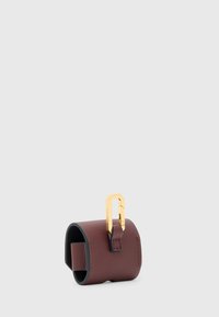 Accessorio in pelle di un profondo color bordeaux con una superficie liscia; presenta una chiusura in metallo dorato e una forma cilindrica minimalista.