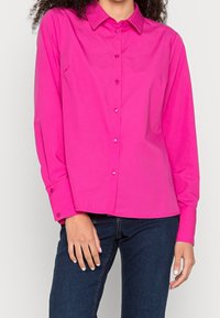 Fuchsia långärmad skjorta med knappar och krage, med en jämn textur och formsydd design, kombinerad med mörka jeans.