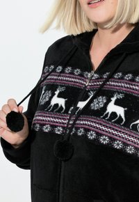 Sort fleece zip-up hoodie med et mønstret yoke med hvide rensdyr, lyserøde detaljer og sorte pom-pom snor.