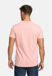 Light pink cotton t-shirt with short sleeves, round neckline, and a straight hem. Worn with blue denim jeans, showing an uncluttered background.