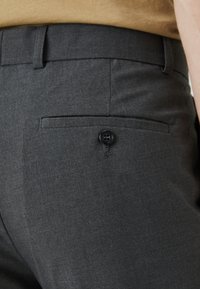 Gray trousers featuring a smooth texture, a back pocket with a black button closure, and a tailored design.