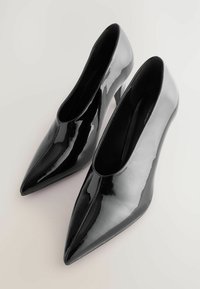 Zapatos de tacón alto negros brillantes con un diseño de punta. Acabado de charol suave y lados abiertos. Silueta elegante con tacones altos.