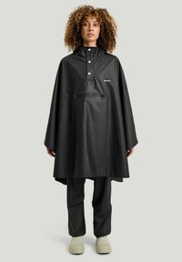 Svart vattentät poncho med huva, tryckknappar och en framficka. Har en avslappnad passform och en slät textur. Enkel, funktionell design.