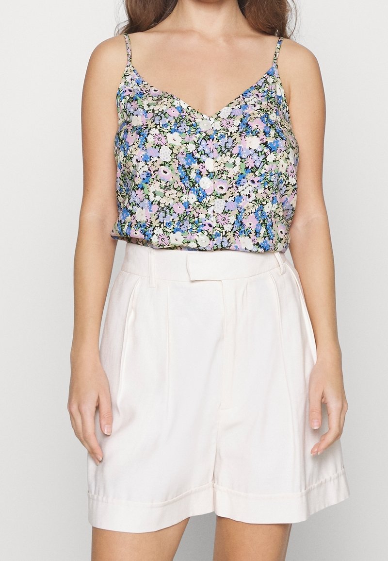 Débardeur floral avec des fleurs vertes, roses et bleues. Tissu léger, décolleté en V et fines bretelles. Associé à un short taille haute de couleur rose pâle.