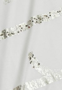 Weißer Stoff mit silbernen Paillettenstreifen, die diagonal verlaufen. Die Textur ist glatt mit reflektierenden Details und einem subtilen Glanz.