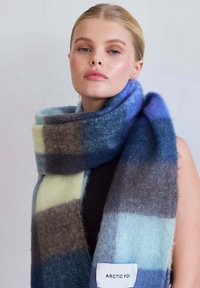 Wollen sjaal met een blauw, grijs en roomkleurig ruitpatroon. Zachte textuur met een label met de tekst "ARCTIC FOX" aan de ene kant.