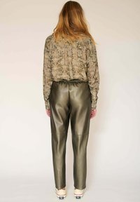 Blouse à manches longues avec un motif floral, associée à un pantalon en cuir synthétique vert olive. Des chaussures décontractées complètent la tenue.