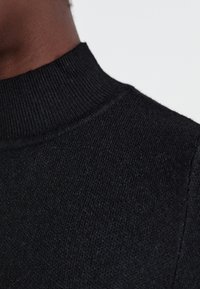 Fekete kötött pulóver magas bordás gallérral. A textúra lágy és enyhén bolyhos, sima felülettel rendelkezik.