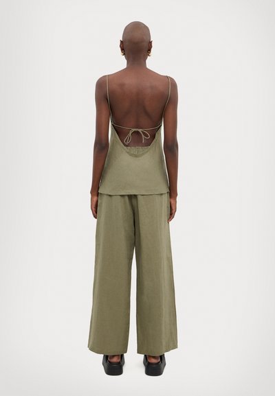 Top senza schienale di colore verde oliva, con spalline sottili e chiusura a fiocco. Abbinato a pantaloni larghi e scomodi dello stesso colore e scarpe con plateau.