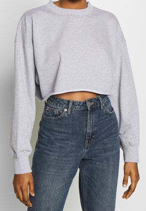 Persoon die een lichtgrijze cropped sweatshirt met lange mouwen en een hooggetailleerde blauwe spijkerbroek draagt.