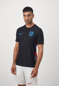 Black short-sleeve sports jersey featuring blue Nike logo and England crest, with textured fabric and colorful graphic accents on the sides.
