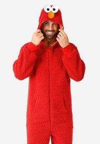 Pijama de forro polar rojo con cremallera en la parte delantera, que presenta una capucha decorada con grandes ojos y una nariz naranja, además de dos bolsillos frontales.