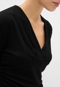 Top aderente nero con scollatura a V profonda e dettagli a pieghe. Tessuto morbido e arricciature laterali sottili, che enfatizzano una silhouette strutturata.