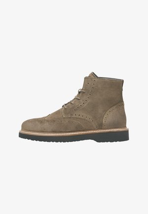 Bottes cheville en daim marron avec détails perforés, bout arrondi et surpiqûre blanche contrastante le long de la semelle. Semelle en caoutchouc noire pour une meilleure adhérence.