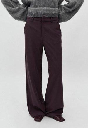Personne portant un pantalon large violet foncé et des chaussures pointues foncées, associées à un pull gris duveteux à manches longues.