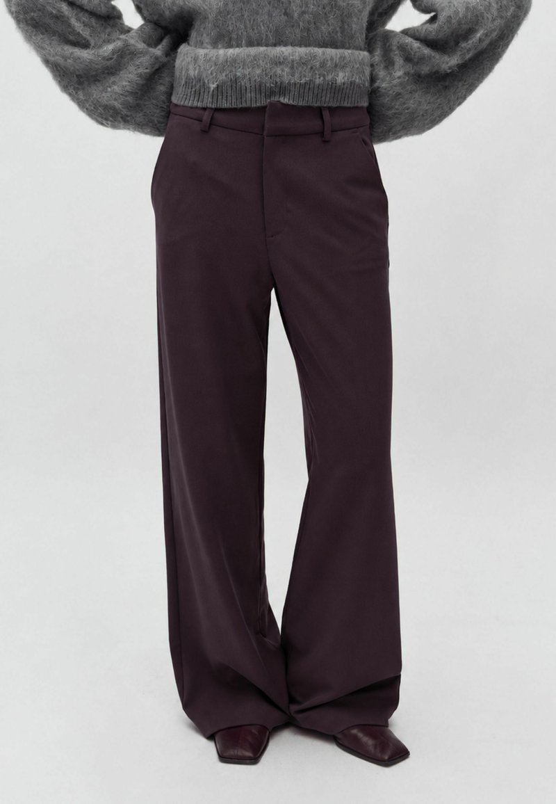 Personne portant un pantalon large violet foncé et des chaussures pointues foncées, associées à un pull gris duveteux à manches longues.