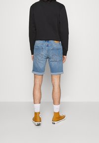 Farkkutrikoot, joissa käännetyt kankaat, vaaleansininen väri, yhdistettynä valkoisiin sukkiin ja keltaisiin korkeisiin tennareihin, päällä musta huppari.