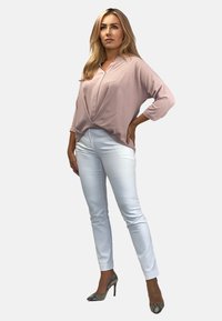 Jasnoróżowa bluzka o luźnym kroju i rękawach 3/4, zestawiona z dopasowanymi białymi spodniami i wzorzystymi szpilkami. Gładka faktura podkreśla design.