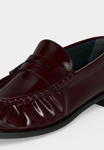Mocassin en cuir bordeaux foncé brillant avec des détails cousus et une semelle basse noire, présenté en gros plan sous un angle.