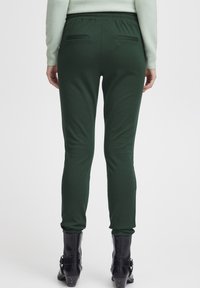 Green elastic-waist pants with slim fit and two back pockets, paired with black ankle boots and a light-colored sweater.