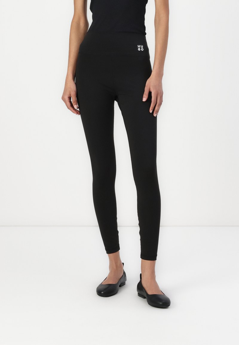 Zwarte leggings met een hoge tailleband met witte "HUGO" branding, gemaakt van een soepele, rekbare stof voor comfort en flexibiliteit.