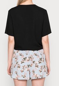 Blusa nera a maniche corte abbinata a pantaloni corti floreali azzurri con accenti rosa e verdi, realizzata in un tessuto morbido e leggero.