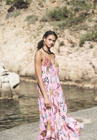 Robe maxi rose à motifs floraux avec fines bretelles, ornée de broderies vives en vert, rouge et jaune. Tissu léger, design fluide.