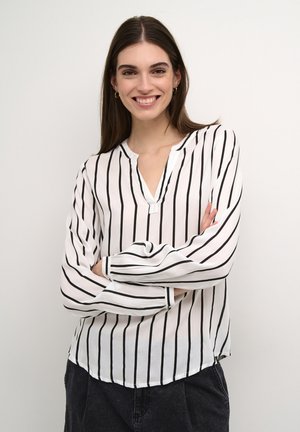 Blusa blanca con rayas negras verticales, escote en V, mangas largas con puño y dobladillo ligeramente curvado. Tejido ligero, corte relajado.