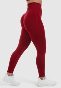 Rode hoge taille legging van rekbare stof, met een aansluitend ontwerp en een gladde textuur. Draagt met witte sportschoenen.