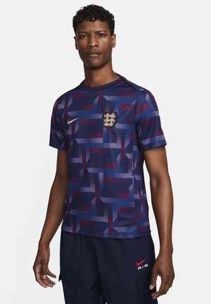Short-sleeve football shirt in dark blue with abstract purple and maroon pattern. Features a gold Nike logo and an embroidered crest on the chest.