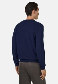 Pull en maille bleu marine avec un col rond, des poignets et une ceinture côtelés, présentant une texture lisse et une coupe classique, vu de dos.